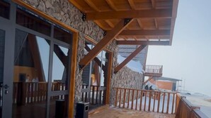 A wooden deck with stone walls, a glass door, and a wooden railing. - Chalet Myler (Yeghipatrush)