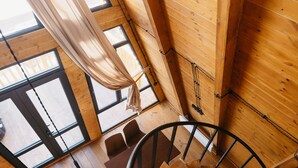 A spiral staircase in a wooden interior with large windows and curtains. - Chalet Myler (Yeghipatrush)