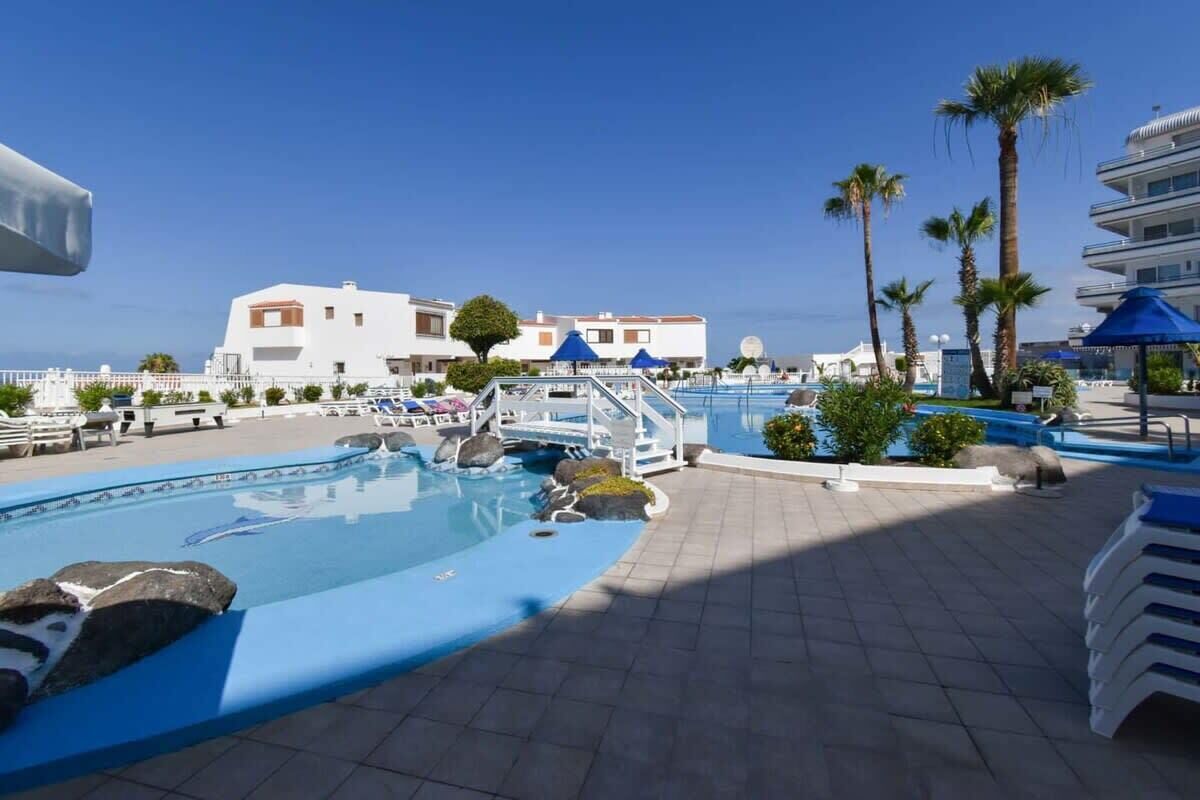 A pool area with clear blue water, lounge chairs, and palm trees.