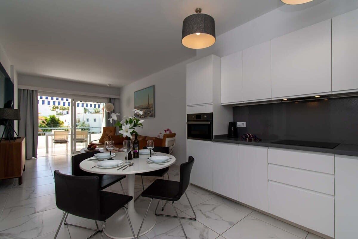 A modern kitchen with white cabinets, a round dining table, and black chairs.