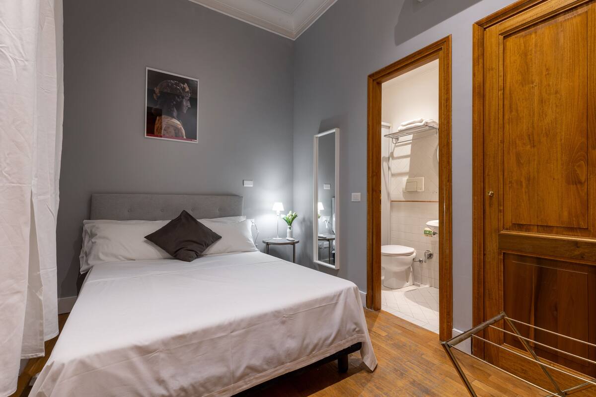 A neatly arranged bedroom with a bed, bedside table, and a mirror.