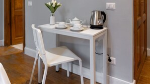 A dining area with a white table and chair, a vase with flowers, a kettle, and a framed picture on the wall. - River61 - Guest House (Rome)