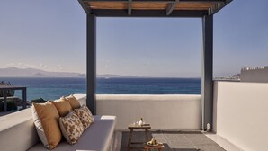 Un balcon avec un canapé, une petite table et une vue sur la mer et les montagnes lointaines.