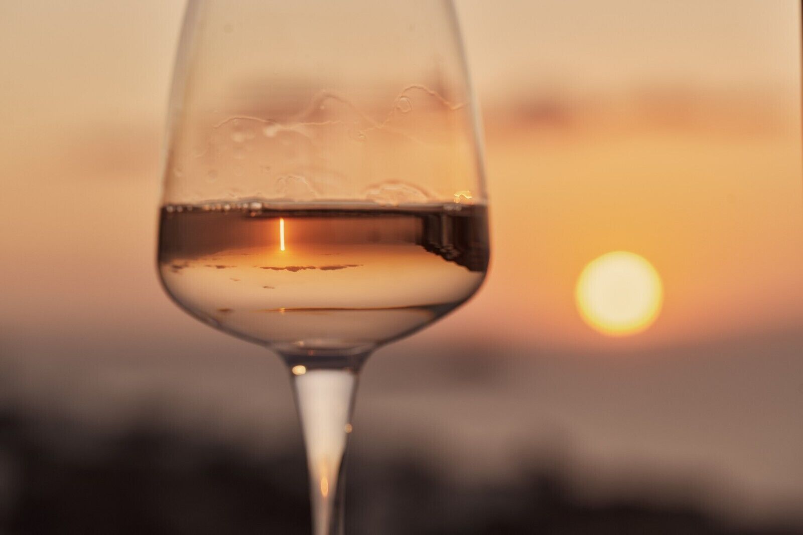 A close-up of a wine glass with a sunset in the background.