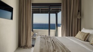 Une chambre dotée d’un grand lit, d’un téléviseur fixé au mur et offrant une vue sur la mer grâce à une porte-fenêtre coulissante.