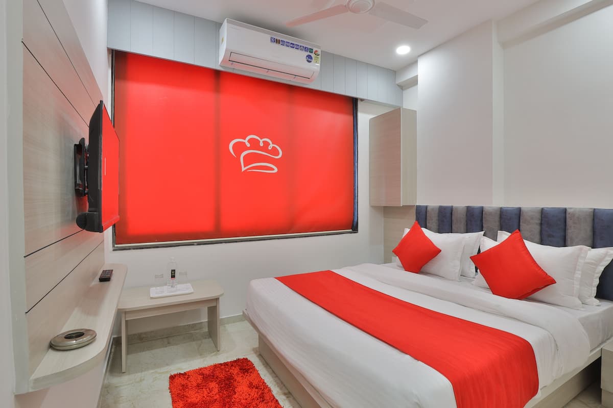 Quarto de hotel moderno com cama grande, detalhes em vermelho, televisão de tela plana e aparelho de ar condicionado.
