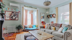 A cozy living room with a sofa, a coffee table, and a large window with curtains. - The Bohemian Suite (Staunton)