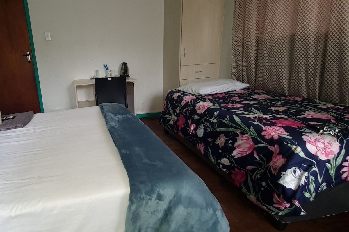 Una habitación de hotel con dos camas, una mesita con hervidor y un armario.