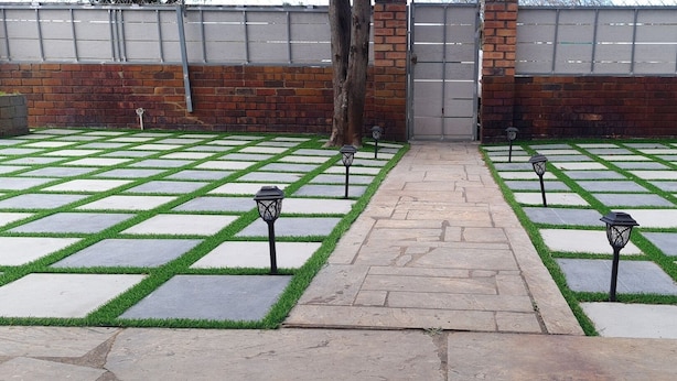 Un sendero pavimentado con un muro de ladrillo y una reja metálica al fondo.