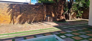 Un jardin avec un mur en briques, un arbre, une piscine et une zone dallée.