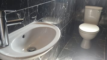 Un baño con lavamanos y retrete blancos, paredes de mármol y grifo cromado.