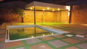 Una piscina con un diseño geométrico de mosaicos, rodeada de muros de ladrillo y una zona techada con iluminación.