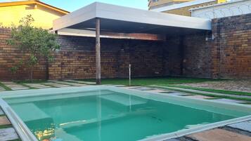 Una piscina con borde de baldosas, rodeada por un muro de ladrillo y una zona cubierta.