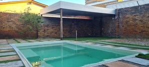 Une piscine dotée d’une terrasse carrelée, entourée d’un mur de briques et d’un espace abrité.