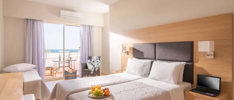 A hotel room with a bed, a desk, a laptop, and a breakfast tray with fruits and juice.