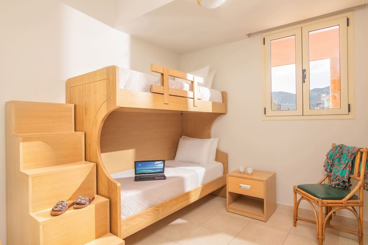 Ein Stockbett mit einem Laptop in der unteren Koje, ein Stuhl mit einer Decke und ein kleiner Nachttisch mit einer Tasse.