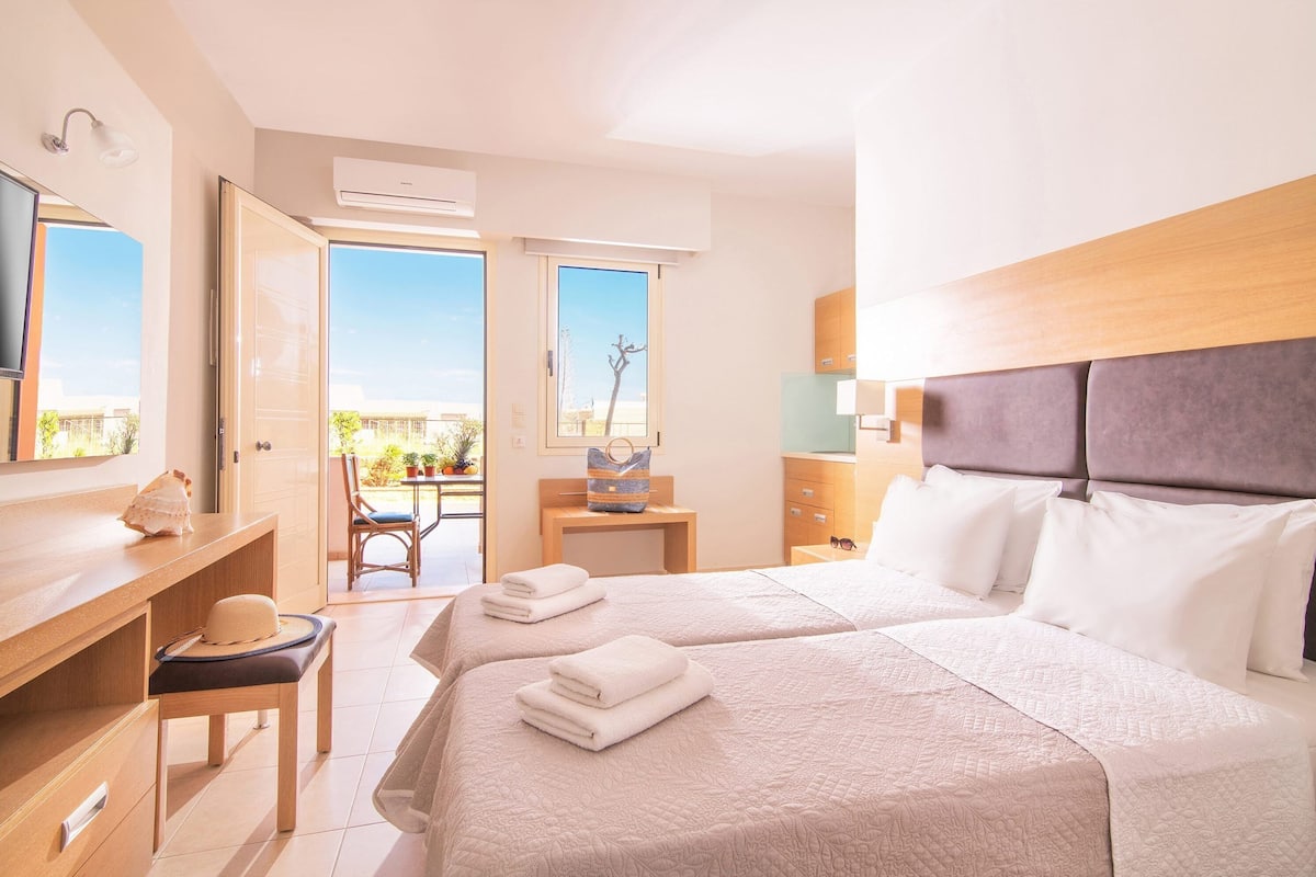 Ein Hotelzimmer mit zwei Betten, einem Schreibtisch, einem Stuhl und Blick ins Freie.