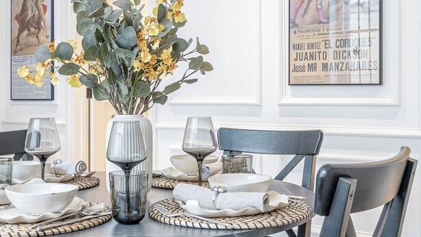 Un coin repas avec une table ronde dressée pour six personnes, entourée de chaises rembourrées.