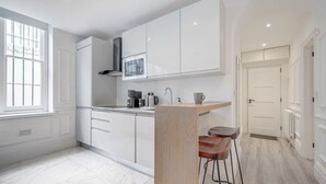 Une cuisine moderne avec des meubles blancs, un four à micro-ondes encastré et un tabouret de bar.