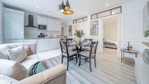 Un salon moderne avec un canapé, une table à manger et des chaises. Il y a un coin cuisine équipé d’un four à micro-ondes et de placards. La pièce est dotée d’un plancher en bois et d’un luminaire au plafond.