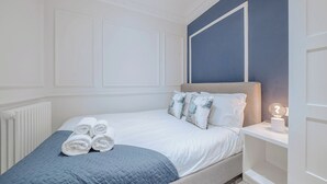 Un lit bien fait, avec des serviettes pliées, une lampe de chevet et un mur d’accent bleu.
