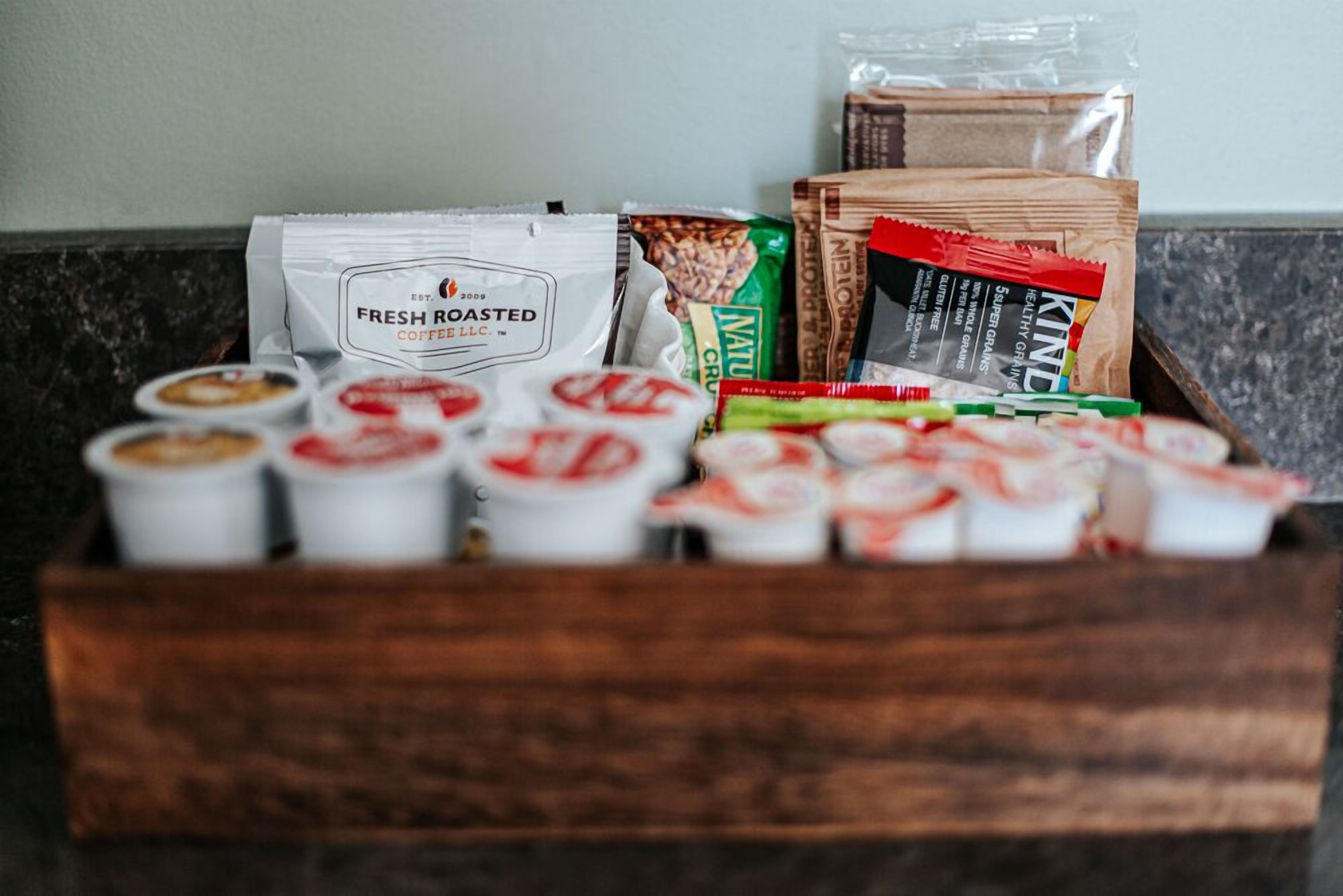 A wooden box containing coffee pods, a bag of Numi tea, and a package of KIND granola.