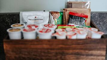 A wooden box containing coffee pods, a bag of Numi tea, and a package of KIND granola.