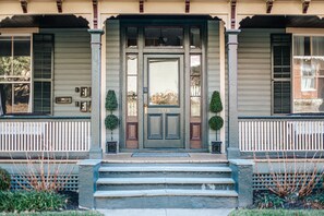 A two-story house with a front porch, a central door with a number, and two small trees on either side. - The Bons Amis Suite (Staunton)