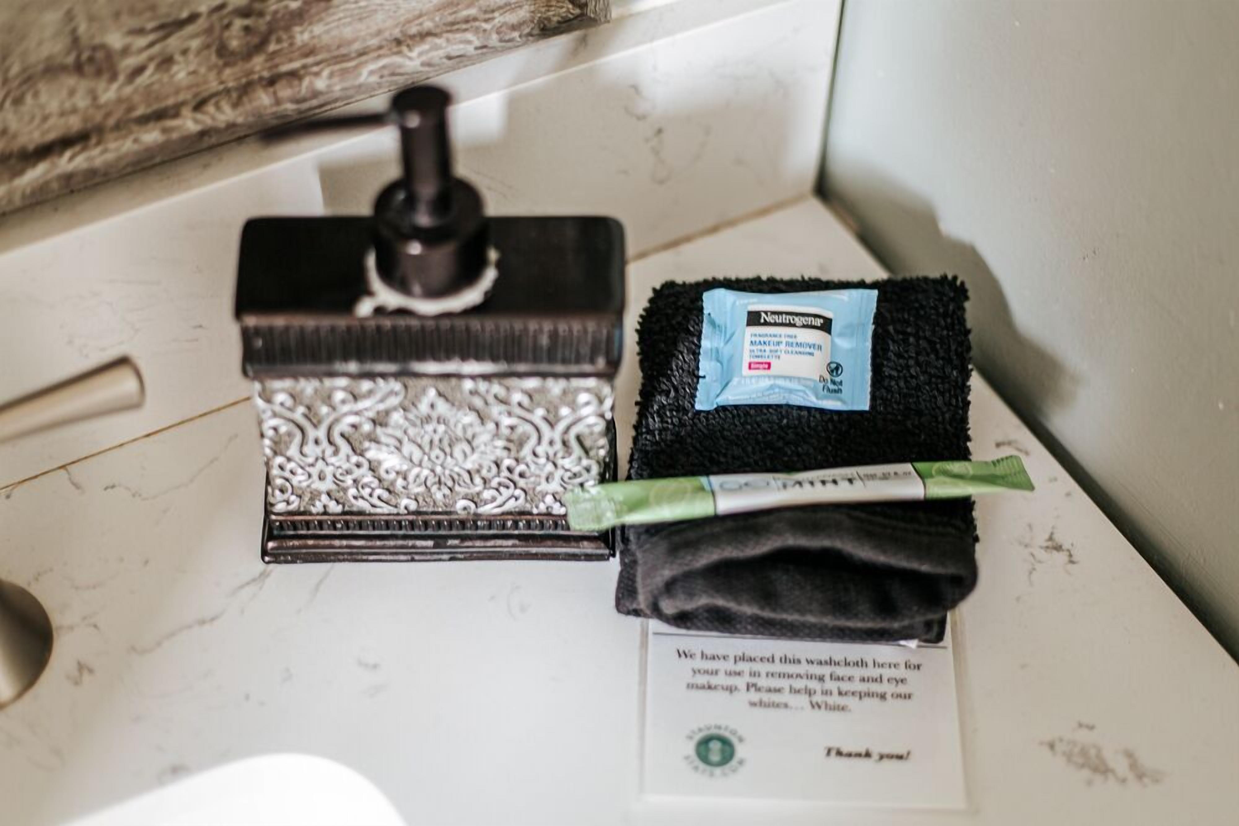 Un lavamanos de baño con un espejo decorativo, una esponja negra y una bolsita de quita maquillaje.