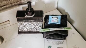Un lavamanos de baño con un espejo decorativo, una esponja negra y una bolsita de quita maquillaje.