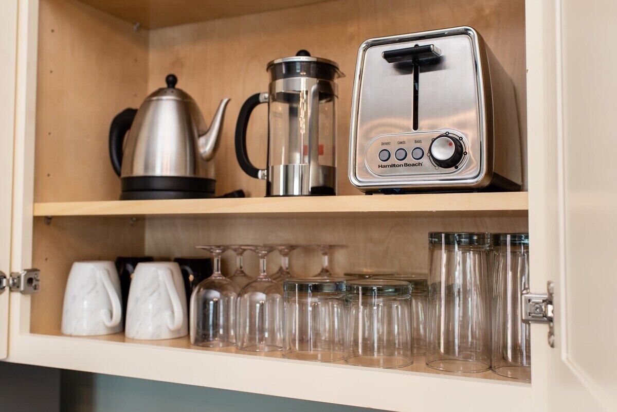 A kitchen with a toaster, a coffee maker, and glassware on shelves.