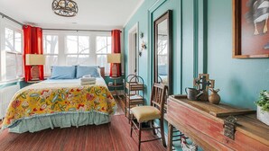 A bedroom with a bed, a wooden dresser, a chair, and a window with curtains. - The Shenandoah Suite (Staunton)