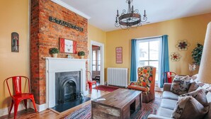 A living room with a brick fireplace, a sofa, a coffee table, and a colorful rug. - The Shenandoah Suite (Staunton)