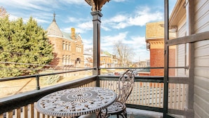A balcony with a wrought iron table and chairs, overlooking a historic building and a wooden fence. - The Shenandoah Suite (Staunton)