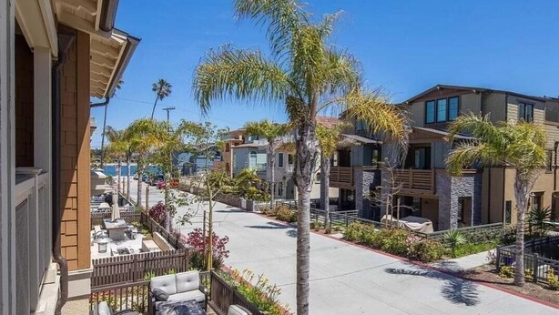 A residential street with modern houses, palm trees, and a clear sky.