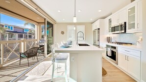 A modern kitchen with white cabinetry, a central island, and a dining area with a view to the outside.