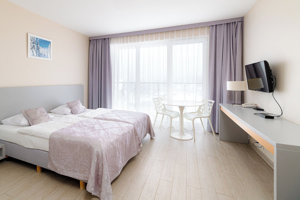 Una habitación de hotel con cama, escritorio con televisor, silla y una mesita.