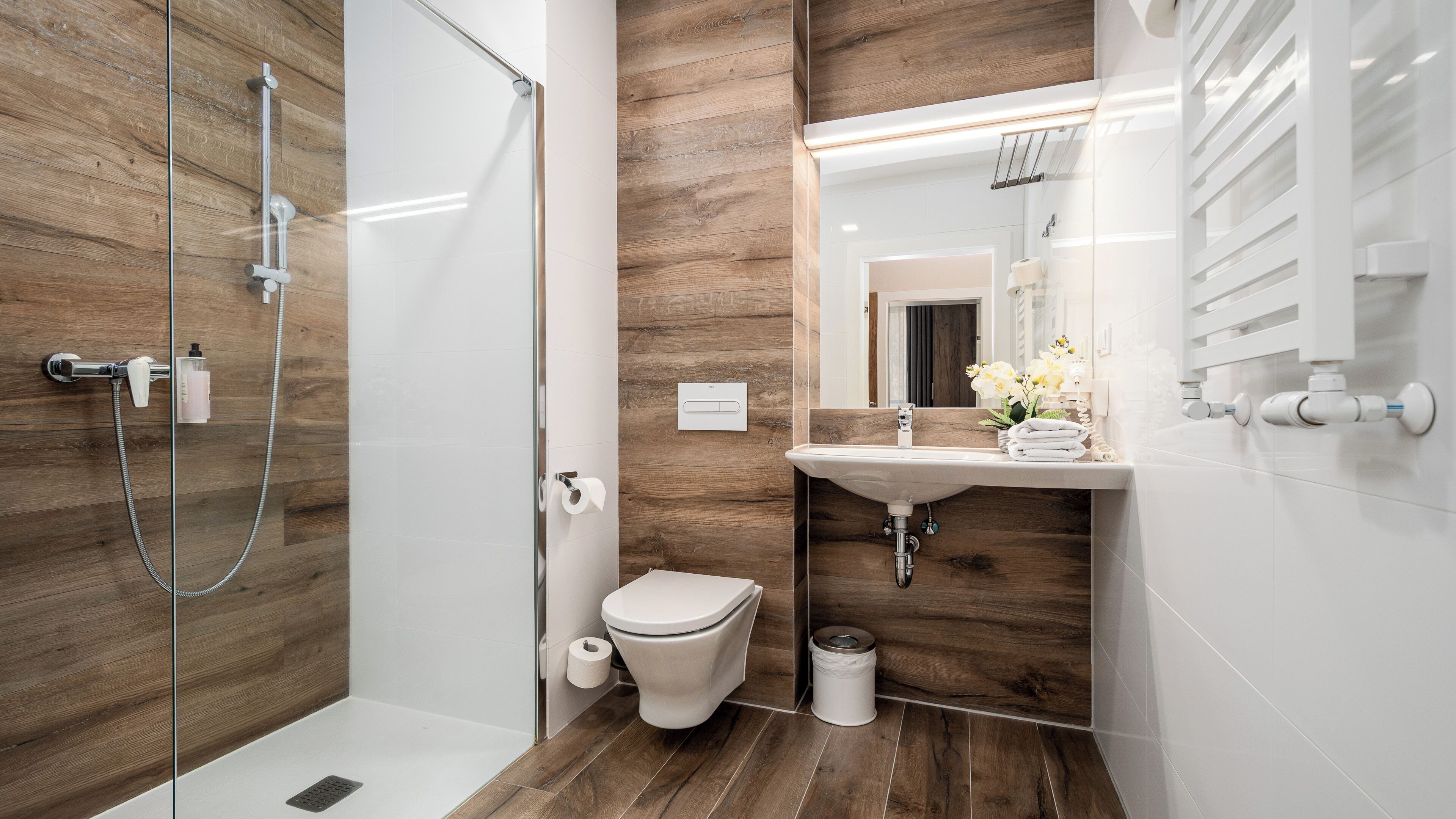 A modern bathroom with a glass shower enclosure, a wooden wall, a white sink, and a toilet.