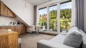 Una cocina moderna con armarios de madera y un comedor. Hay un balcón con vistas a árboles y casas.