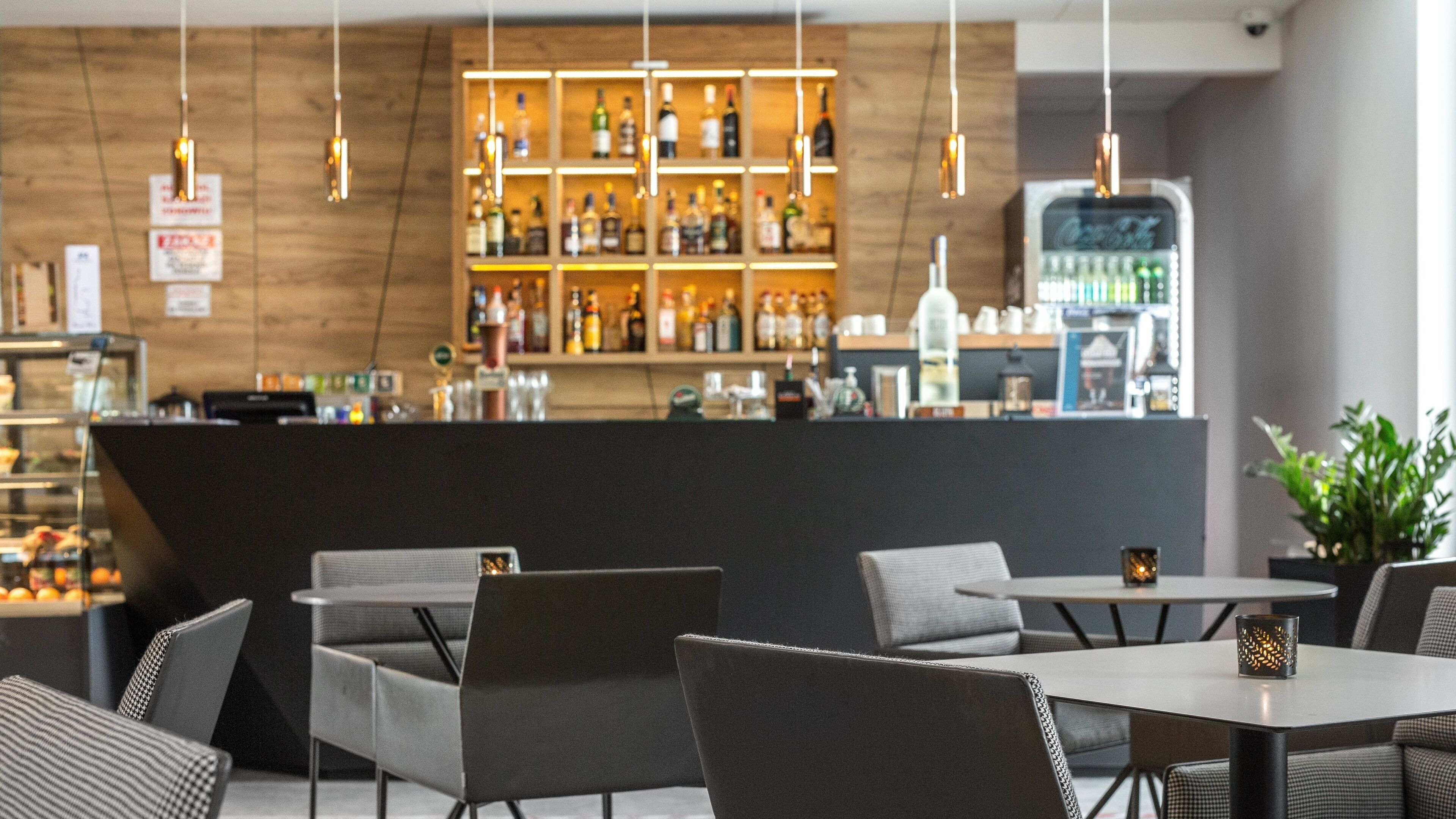 Un espace bar avec des étagères remplies de bouteilles d’alcool, un réfrigérateur Coca-Cola et des sièges avec des tables et des chaises.