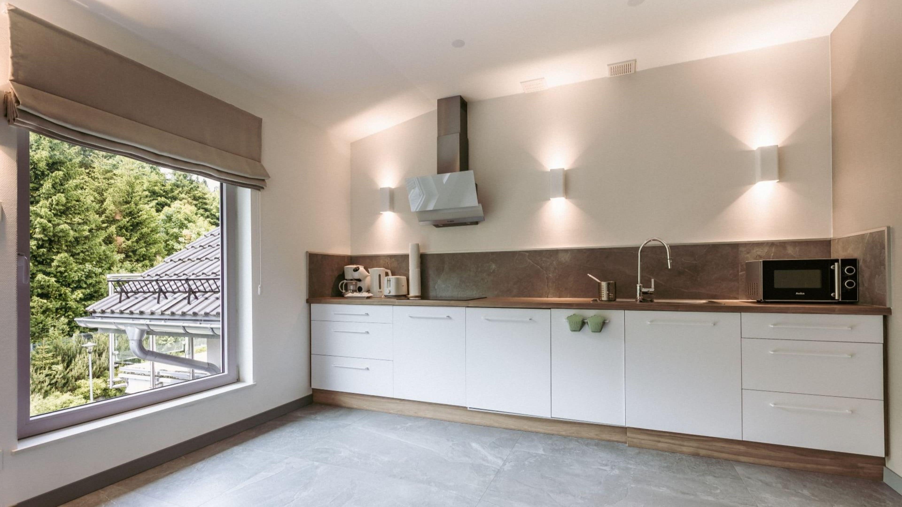 A modern kitchen with white cabinets, a microwave, a coffee maker, and a window with a view of greenery outside.
