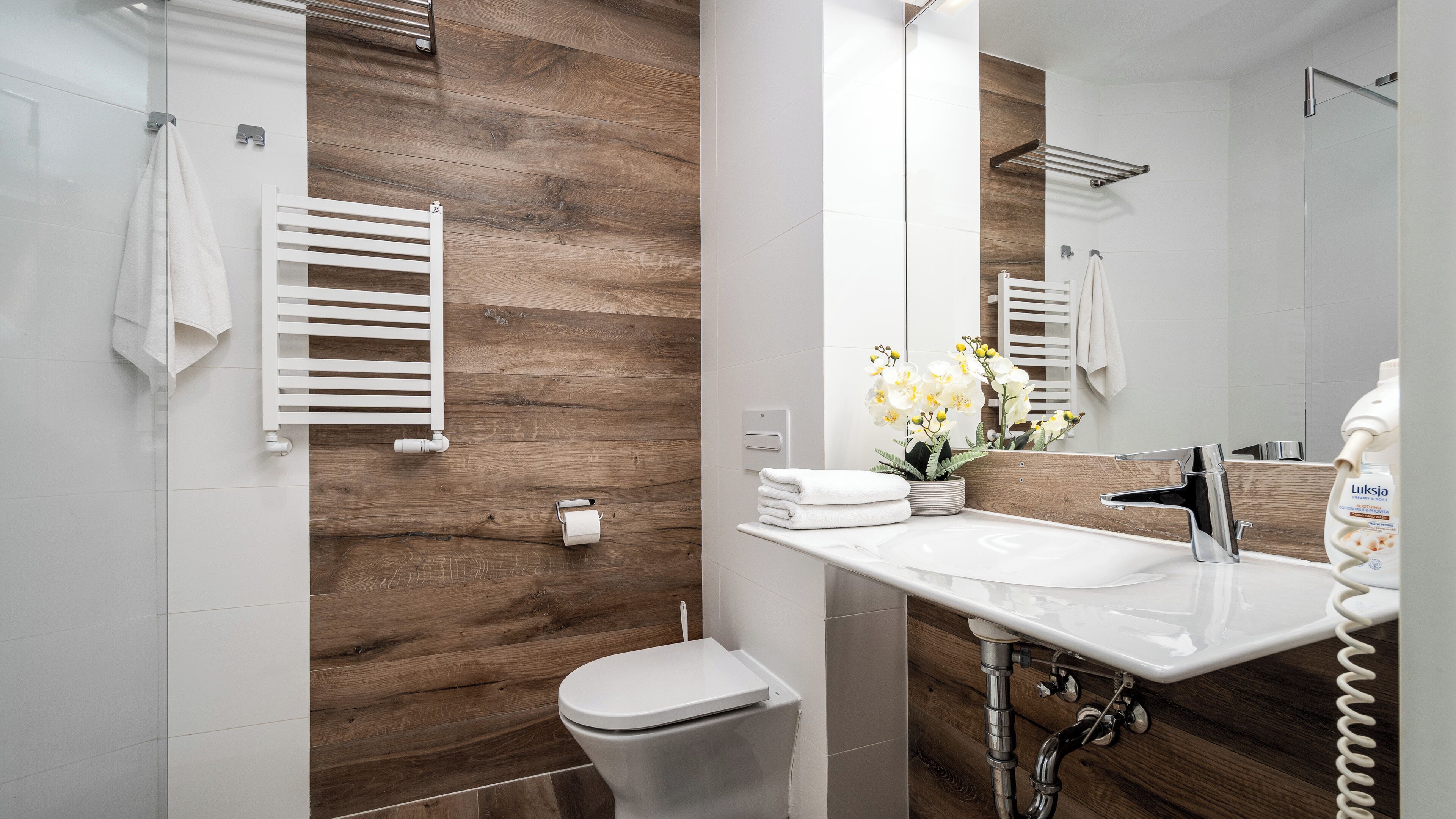 Une salle de bain moderne avec un mur d’accent en bois, un lavabo blanc, des toilettes et un porte-serviettes.