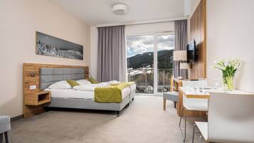 Hotelkamer met een bed, een bureau met stoel, een televisie en een raam met uitzicht op een besneeerd landschap.