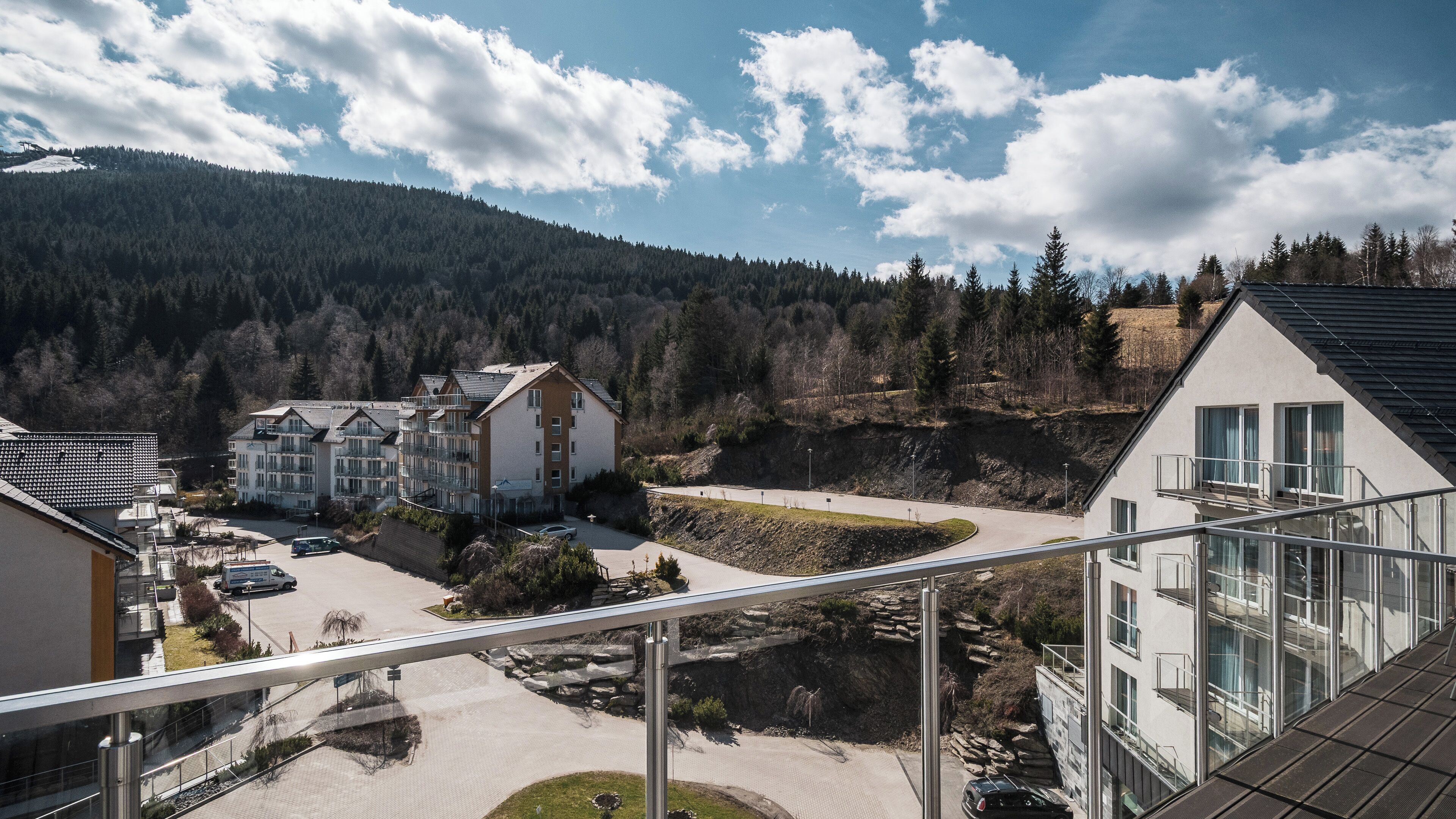 A residential area with modern buildings, a paved road, and a mountainous backdrop.
