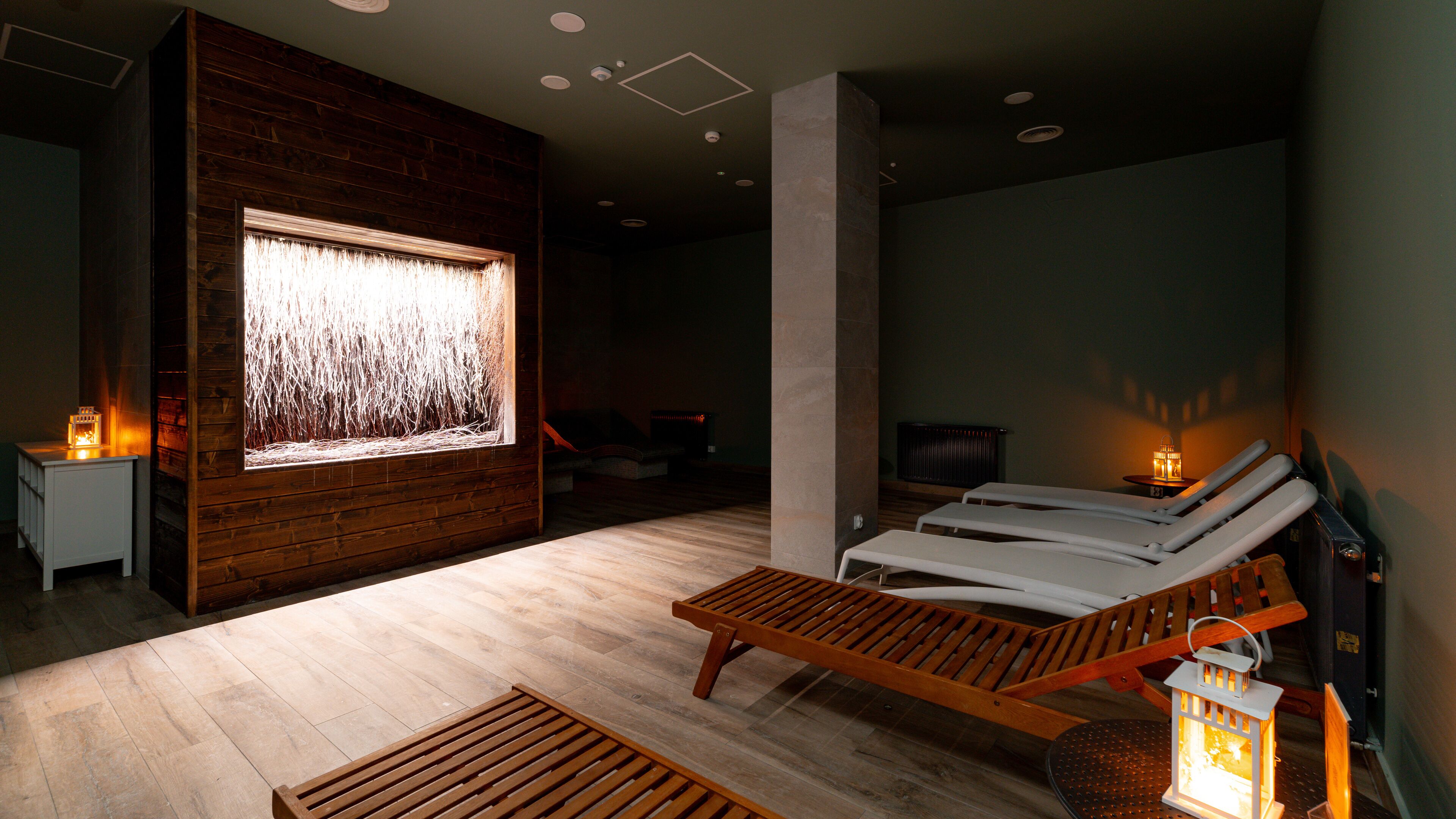 Ein Spa-Raum mit Holzwänden, einer großen Wandanlage mit Wasserspiel und zwei Liegesesseln.