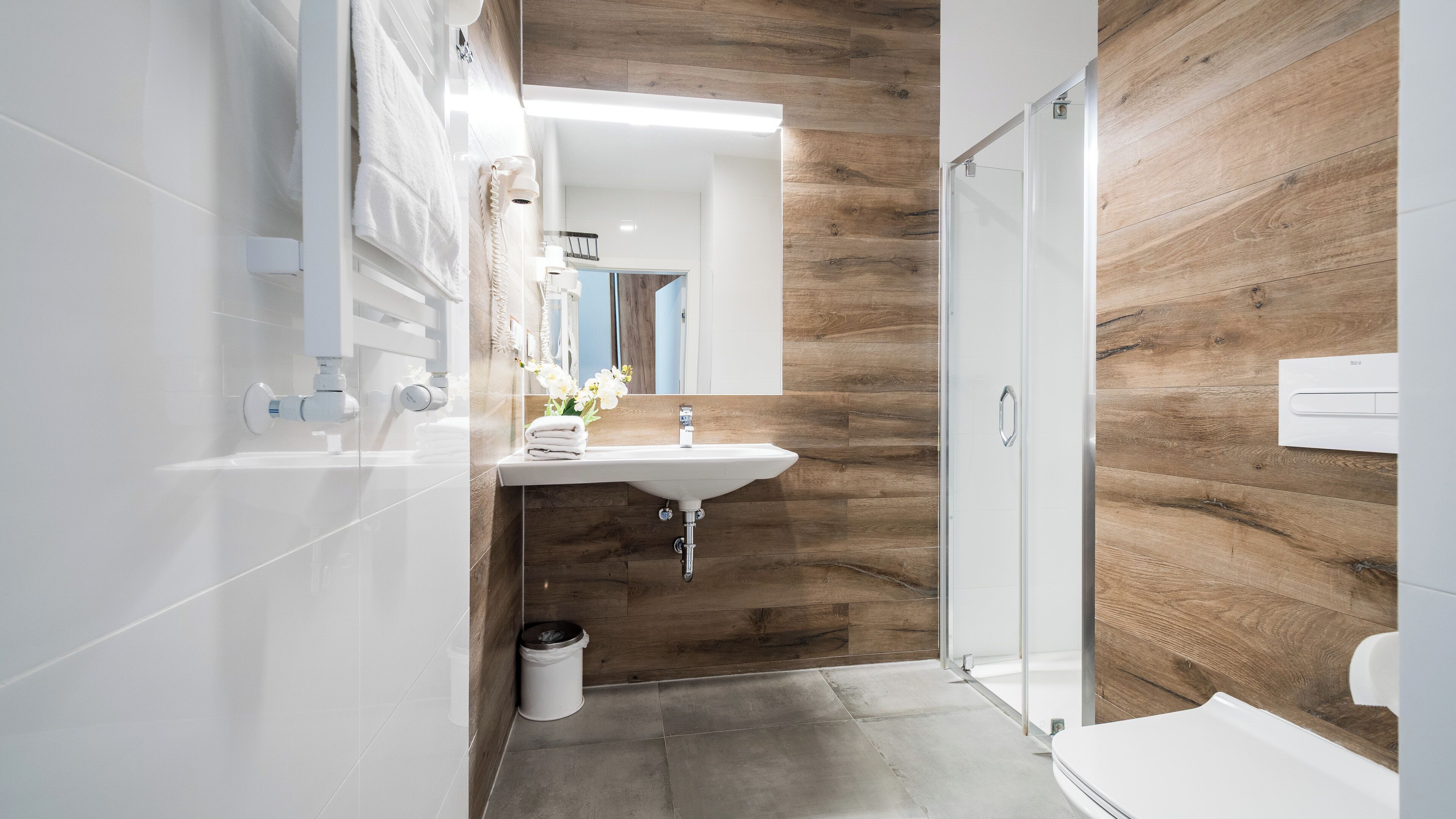 Un baño moderno con una pared de acento de madera, un lavabo blanco y una mampara de ducha de vidrio.