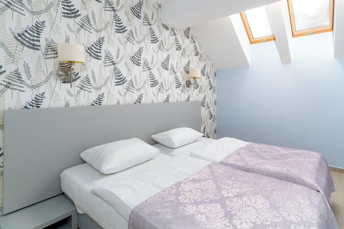 Un dormitorio con cama, dos lámparas de noche, una ventana y un papel tapiz estampado.