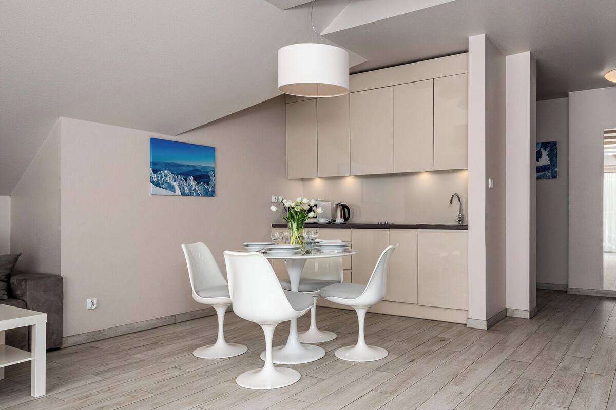 Una cocina moderna con armarios blancos, un comedor con una mesa redonda y sillas blancas, y un cuadro en la pared.