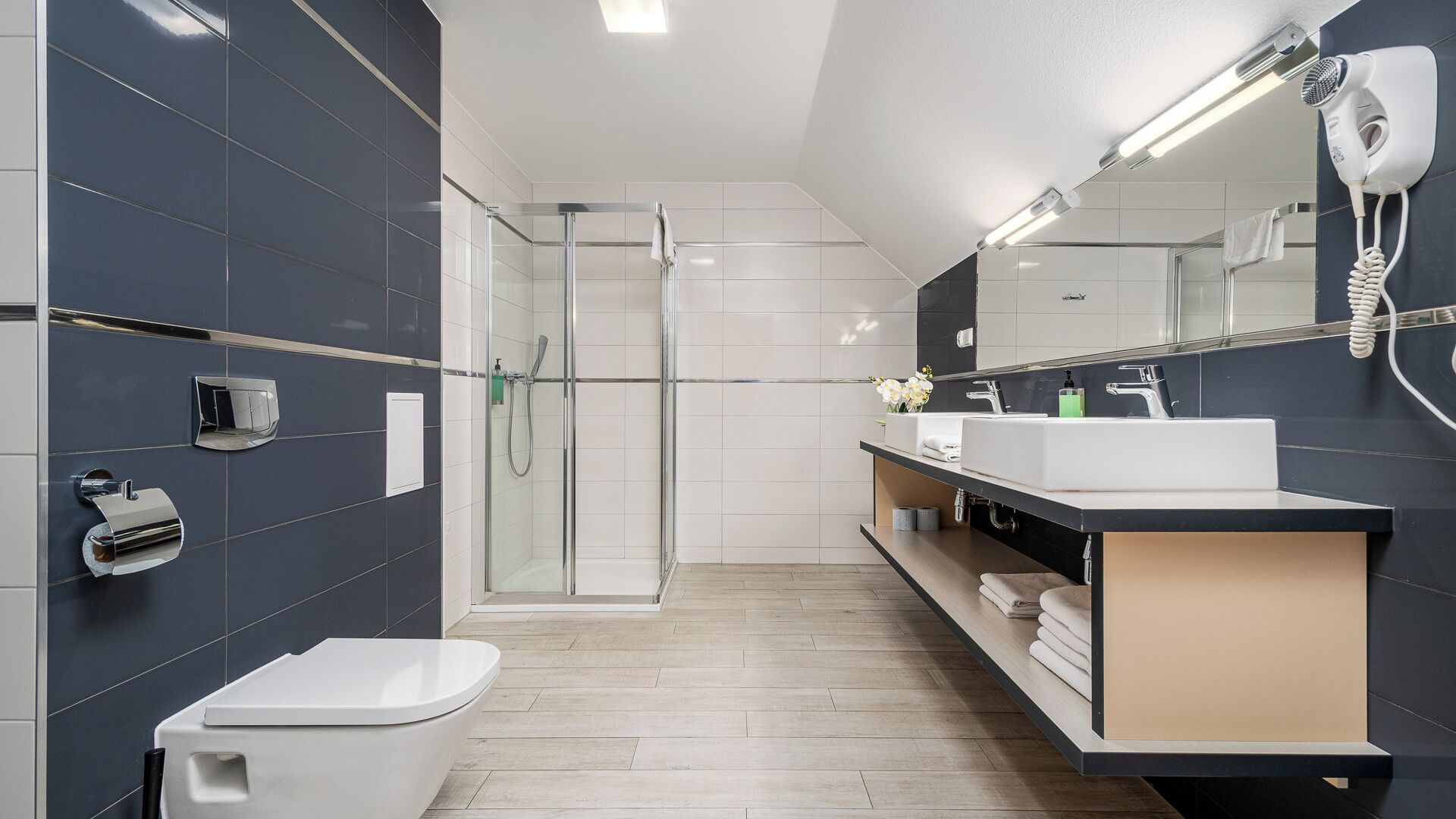 Une salle de bain moderne avec une douche à parois de verre, des toilettes blanches, un meuble-lavabo avec un miroir et un sèche-cheveux fixé au mur.