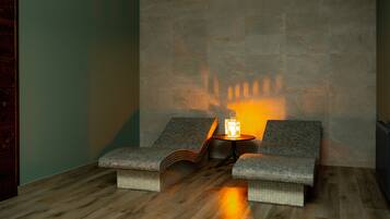 A spa area with two cushioned seating areas, a small table with a lamp, and a tiled wall.